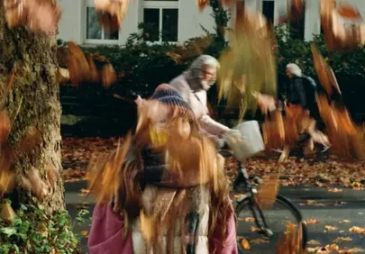 Autumn Hues: Girl Amidst Falling Leaves & Passing Cyclist