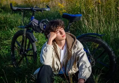 Serene Respite: Young Man Rests by Bike in Sunlit Field