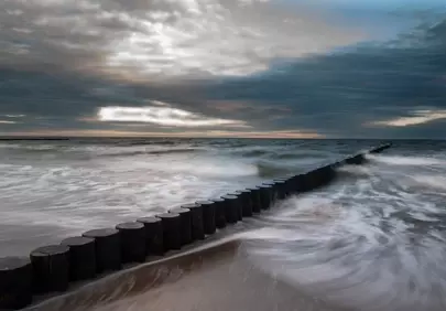 Dramatic Coastal Sunset: Misty Waves and Wooden Groynes