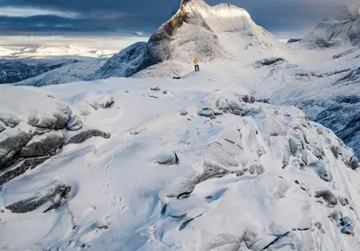 Majestic Winter Ascent: Solitary Hiker on a Snowy Peak