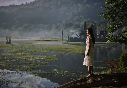 Serene Dawn: Woman Reflecting by an Ancient Indonesian Lake