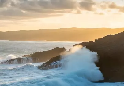 Dramatic Coastal Sunset: Waves Crashing on Rugged Rocks