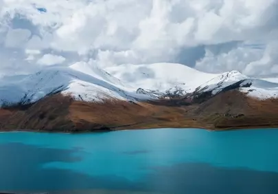 Azure Lake Reflects Snow-Capped Mountains Under Dramatic Sky