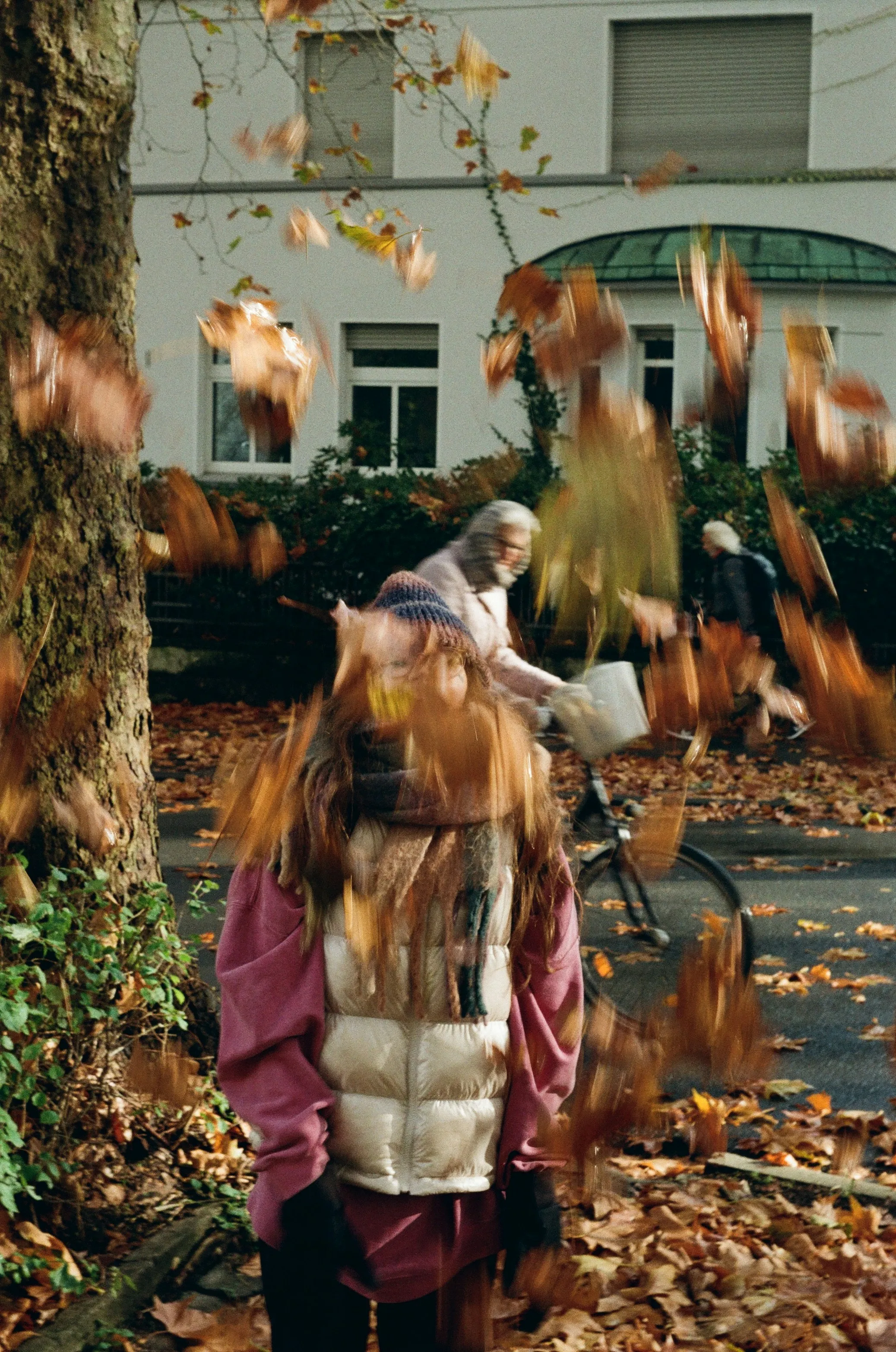 Autumn Hues: Girl Amidst Falling Leaves & Passing Cyclist