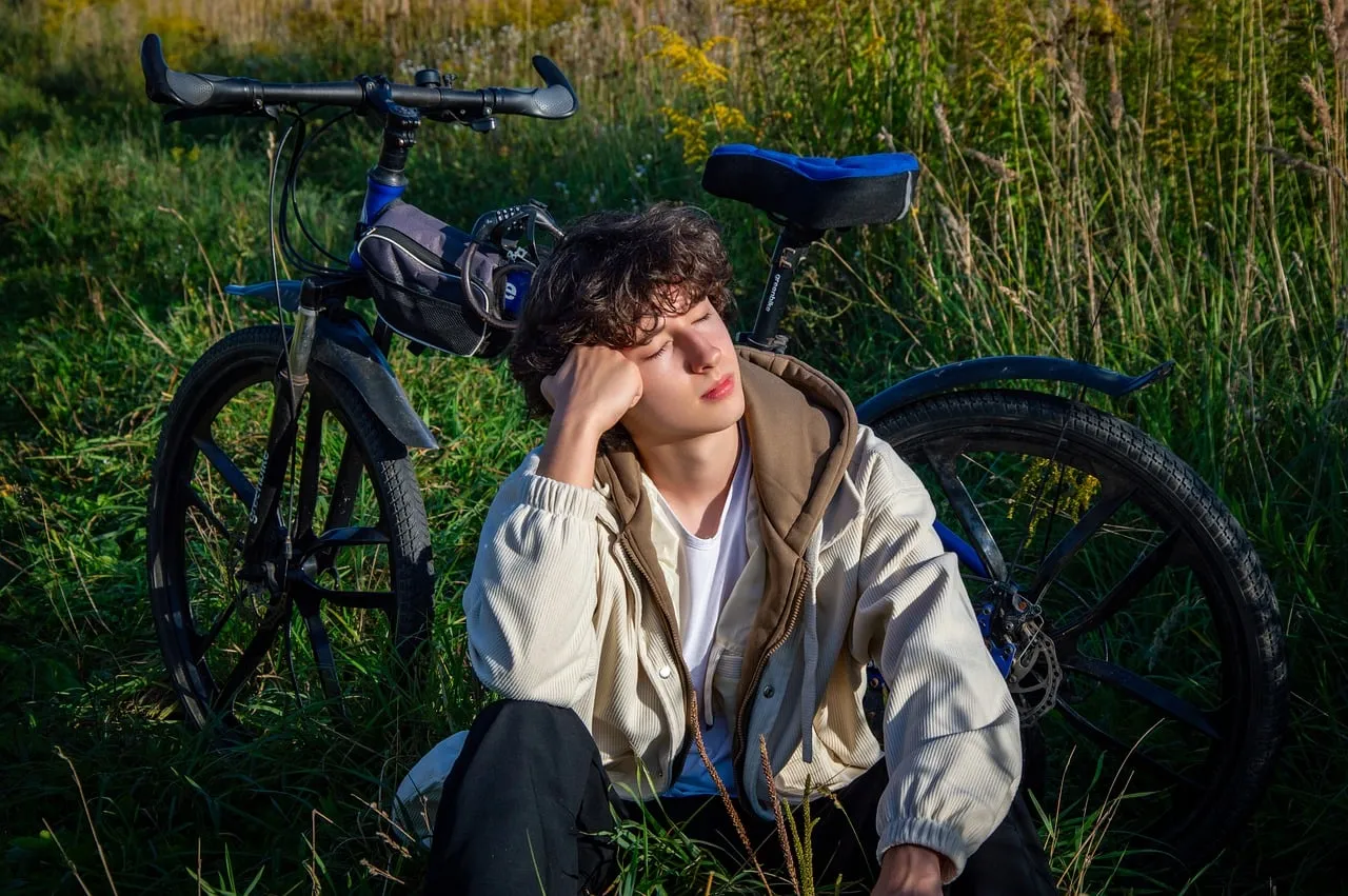 Serene Respite: Young Man Rests by Bike in Sunlit Field