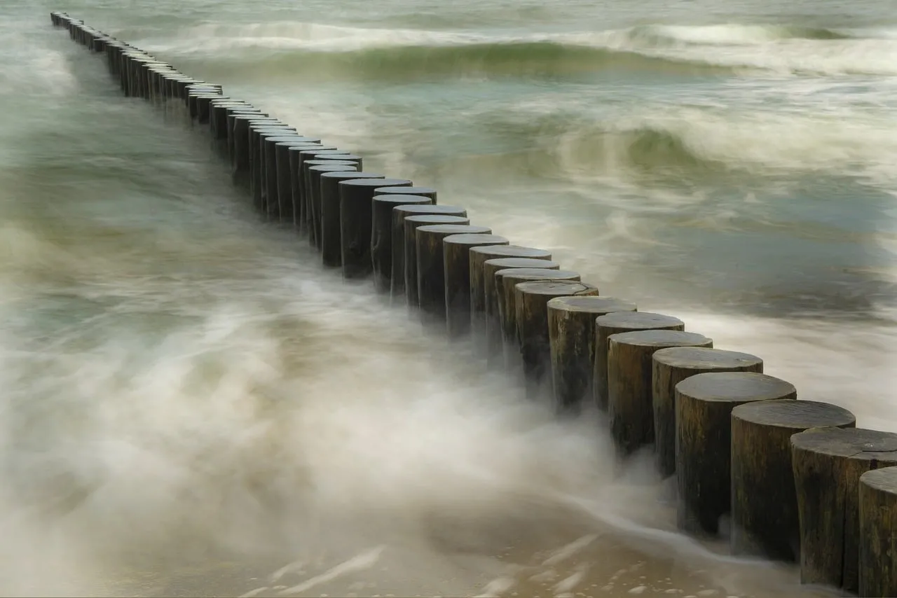 Serene Coastline: Wooden Pillars Battling Foamy Waves