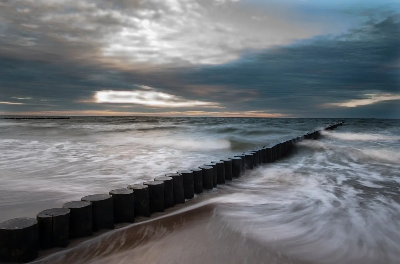 Dramatic Coastal Sunset: Misty Waves and Wooden Groynes