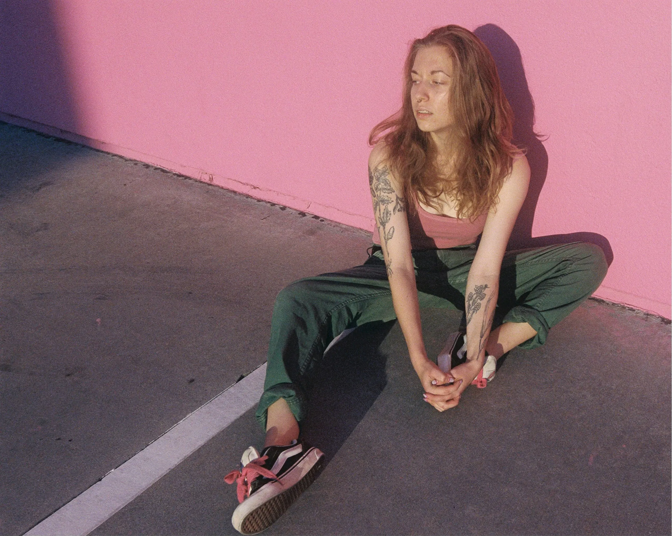 Vibrant Urban Chill: Tattooed Woman by a Pink Wall