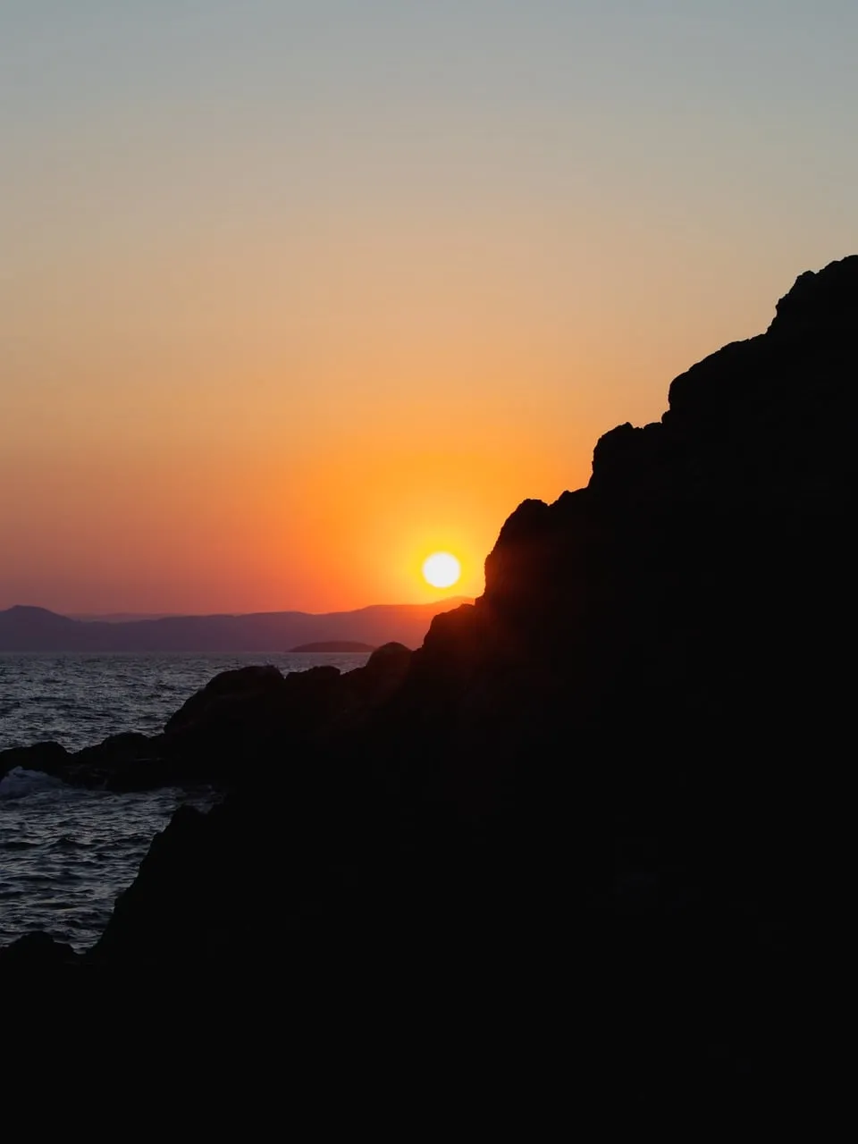 Dramatic Coastal Sunset: Golden Orb Sinks Behind Silhouetted Rocks