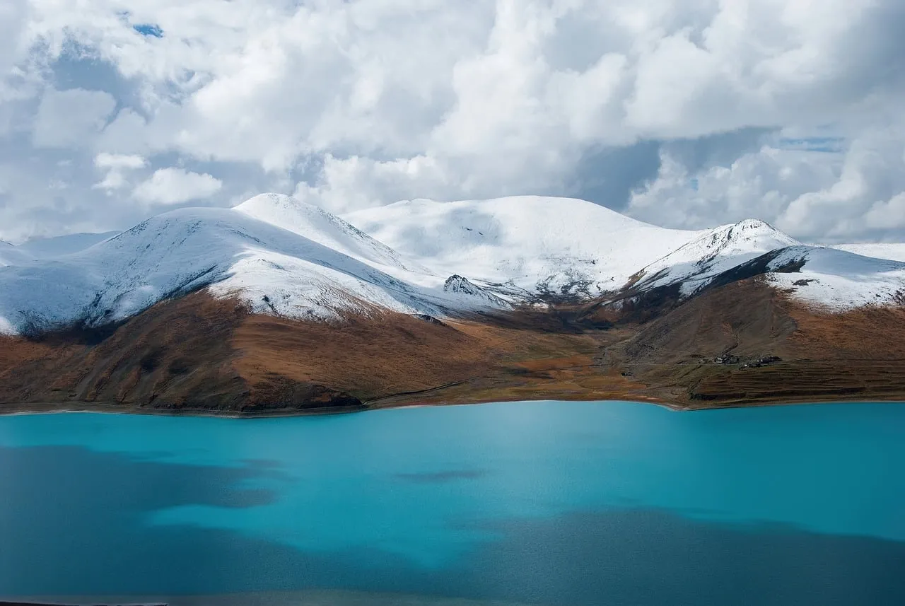 Azure Lake Reflects Snow-Capped Mountains Under Dramatic Sky