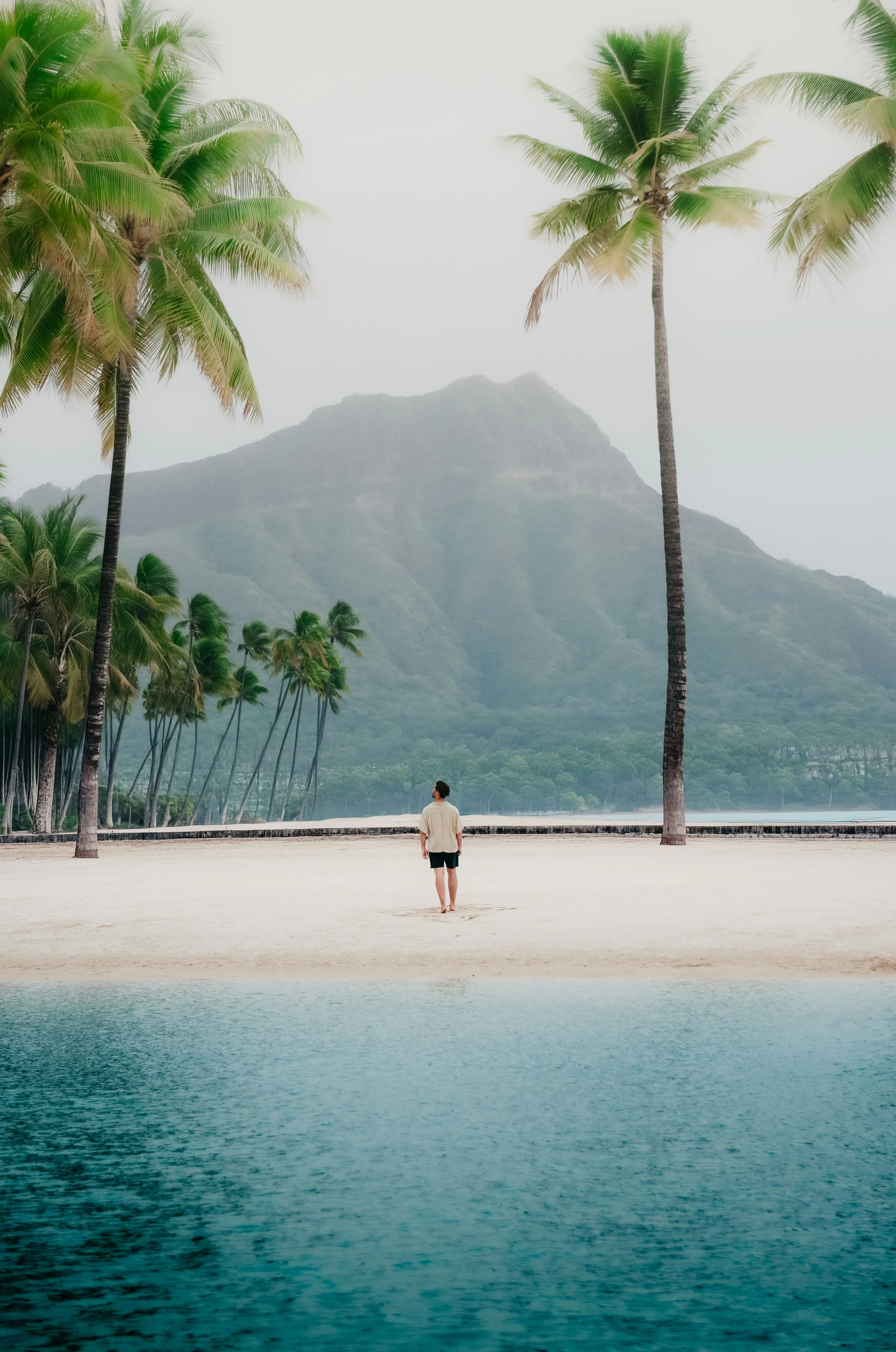 Serene Tropical Escape: Man on a Secluded Beach with Majestic Mountains